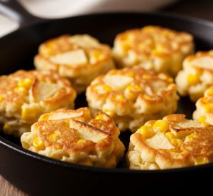 Golden brown corn and apple fritters cooking in a cast iron skillet