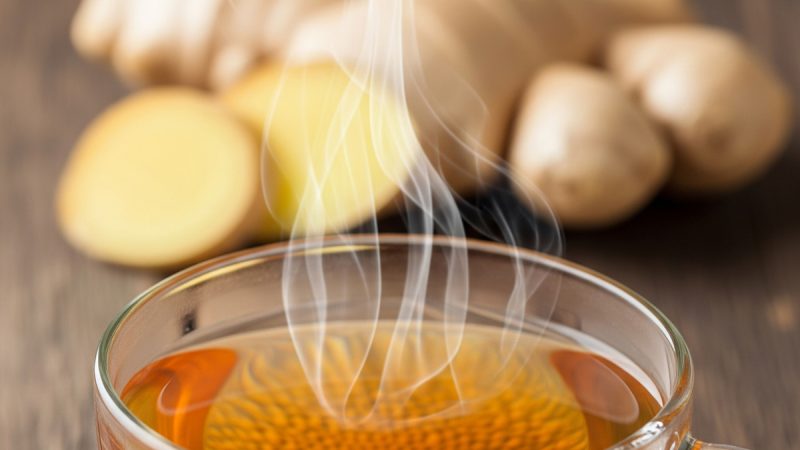 A warm cup of ginger tea with a fresh ginger root in the background.